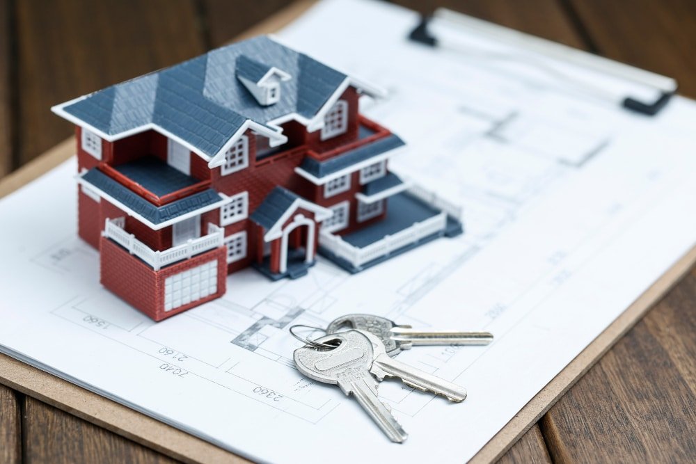 Maquette d'une maison rouge et blanche sur des plans de construction avec des clés à côté.