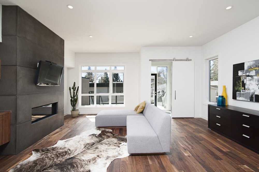 Salon moderne avec cheminée encastrée dans un mur de béton, plancher en bois et grandes fenêtres.