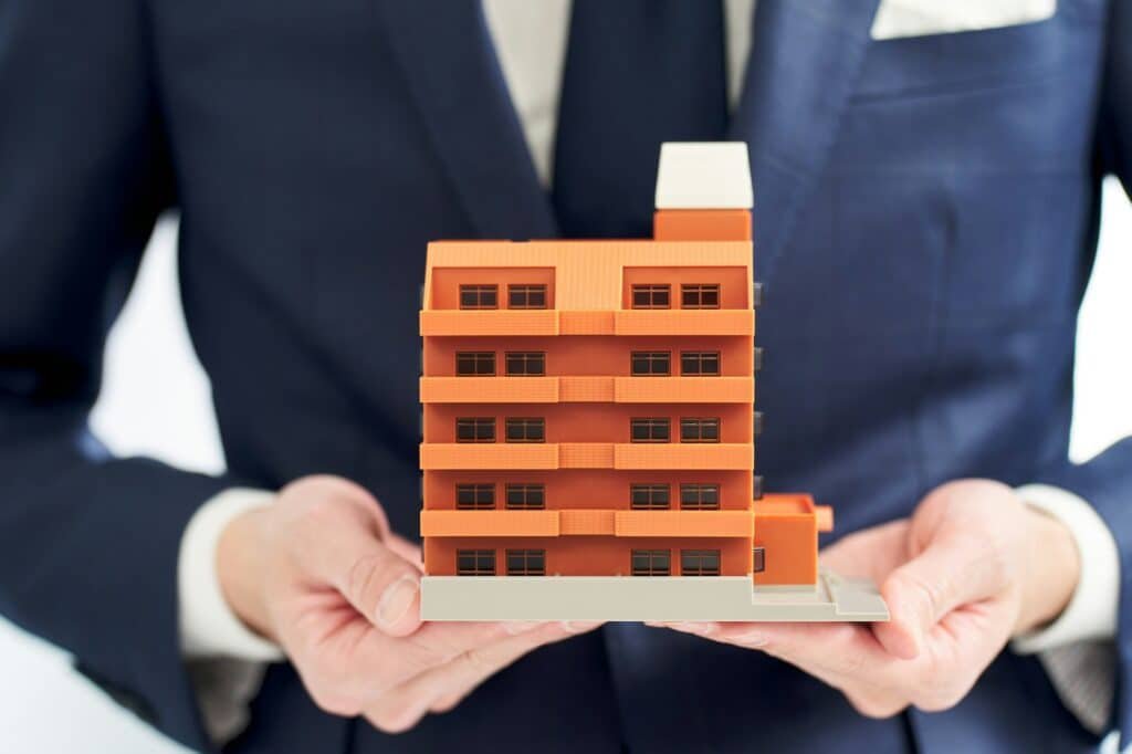 Maquette détaillée d'un immeuble résidentiel orange, dans les mains d'un homme en costume.