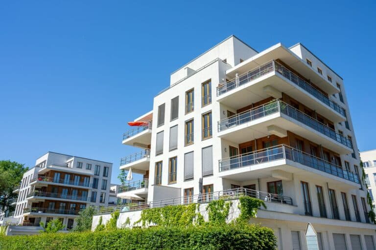 Immeuble résidentiel moderne avec balcons et végétation en façade sous un ciel bleu.