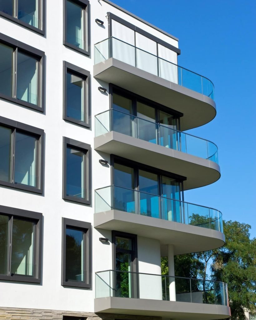 Immeuble résidentiel moderne avec balcons arrondis et garde-corps en verre, façade blanche et fenêtres noires.