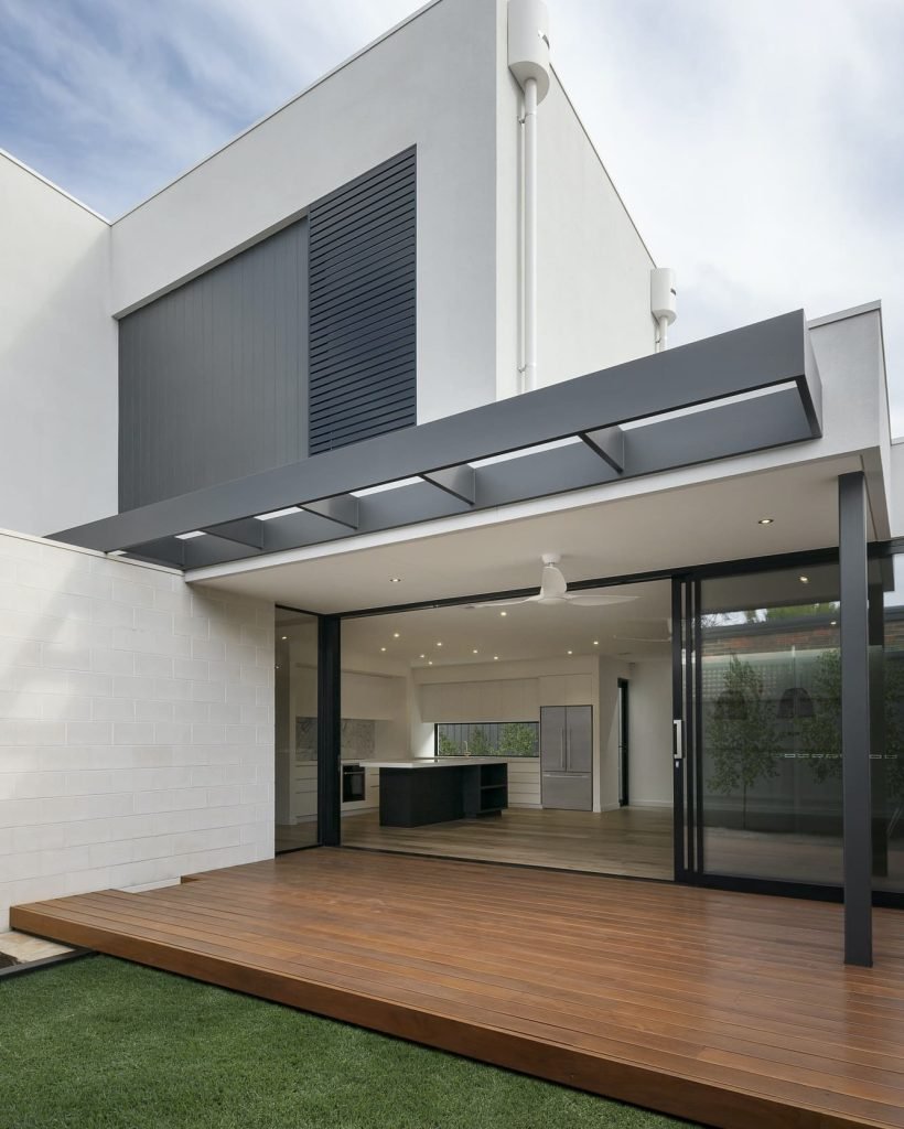 Maison moderne avec grande terrasse en bois, murs blancs et éléments en métal.