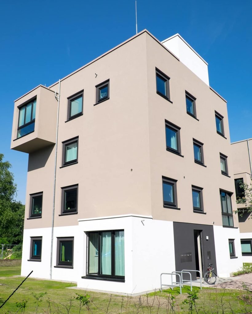 Bâtiment contemporain beige à plusieurs étages avec fenêtres noires et design cubique.