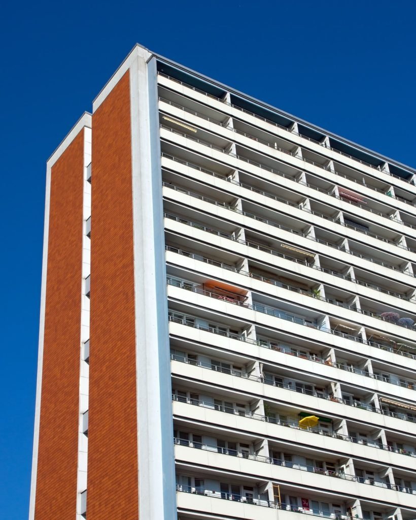 Grand immeuble résidentiel avec façade en brique rouge et balcon blanc, sous un ciel bleu.