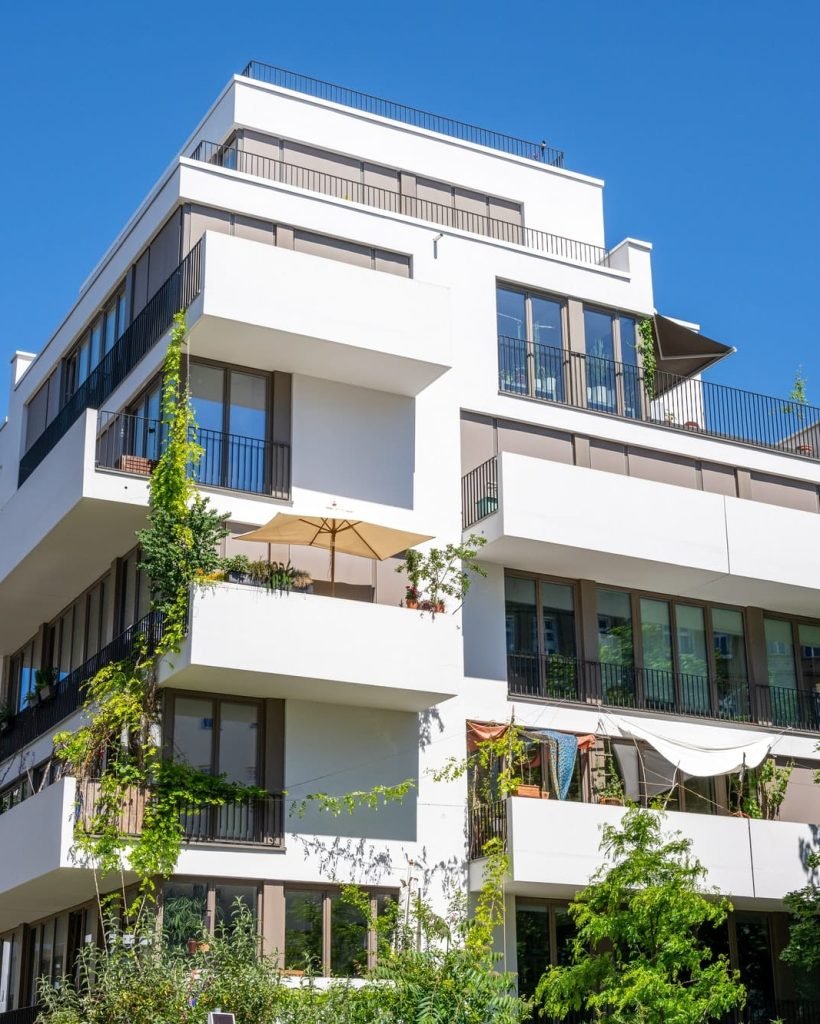 Immeuble blanc moderne avec terrasses verdoyantes et balcons spacieux, ciel clair en arrière-plan.